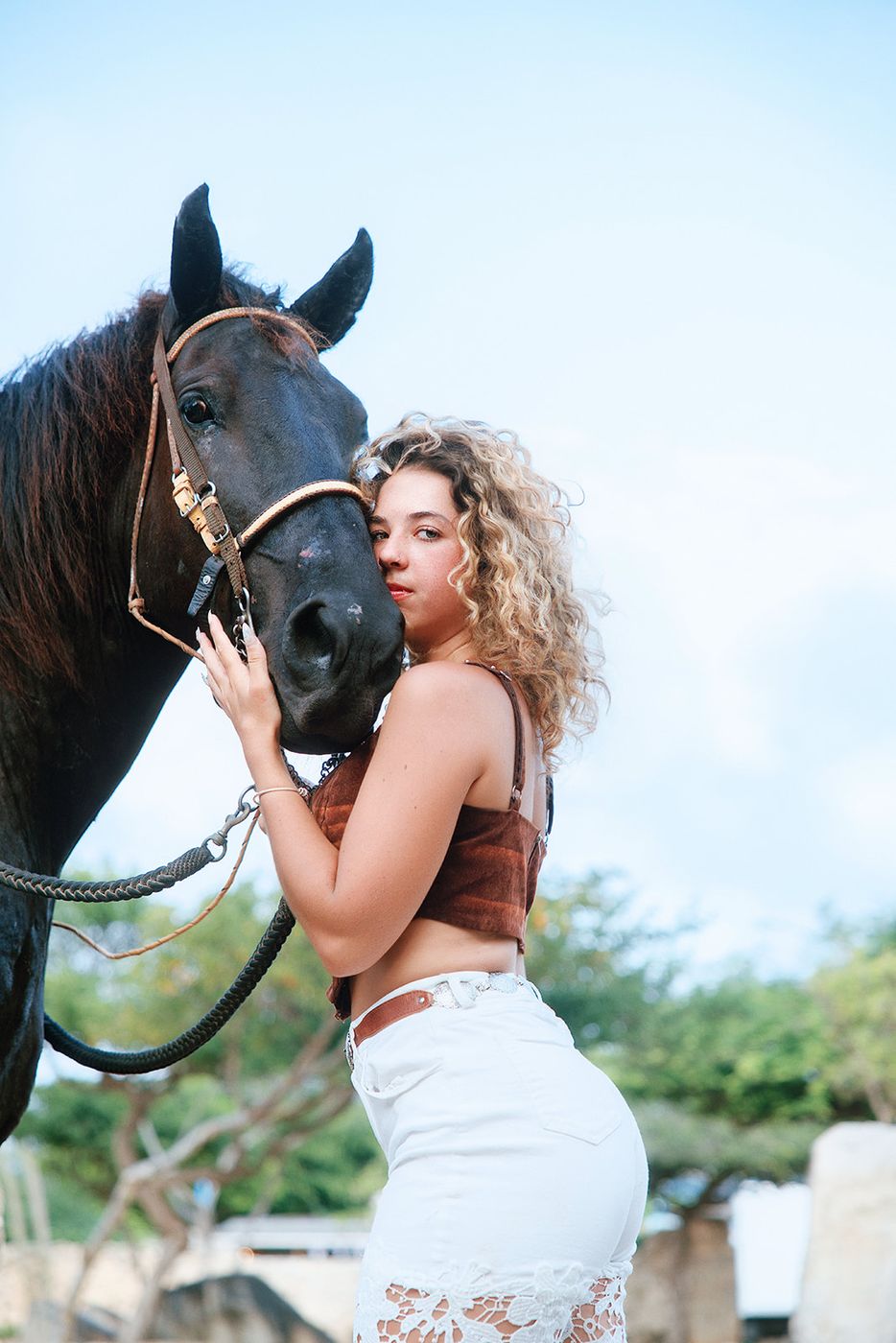 Woman with curly hair embracing a black horse